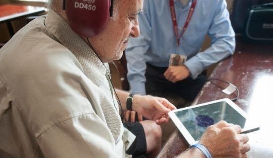 Elderly male with headphones uses iPad screening test