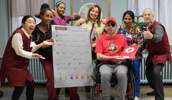 Five woman and two men with thumbs up. One ady is holding a signe with graphics and the center men is in a wheelchair