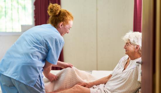 nurse helps senior woman into bed