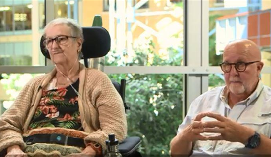 An senior woman in a wheelchair beside a senior man wearing glasses