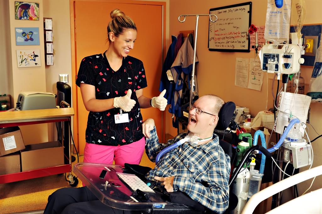Health professional give a thumbs up to a patient in a wheelchair with a ventilator