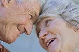 Un couple âgé sourit en se regardant dans les yeux, tête à tête