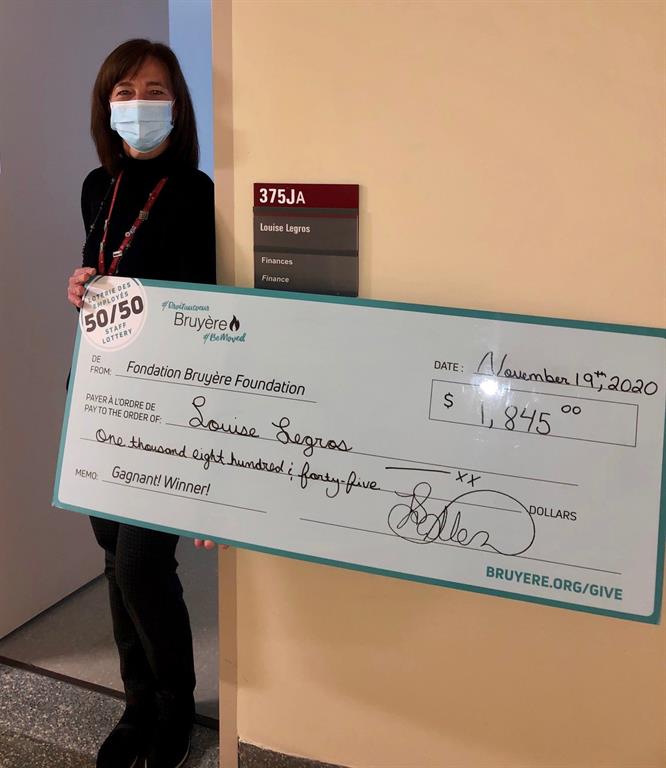 Winner Louise Legros standing outside her office holding a large cheque